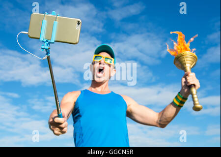 Lächelnde Athlet mit einer Sport-Fackel nehmen ein Selbstporträt mit einem Mobiltelefon auf ein Selfie-stick Stockfoto