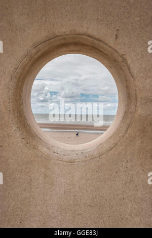 Blick auf Abbildung am Strand durch Kreisloch in Ufermauer Stockfoto