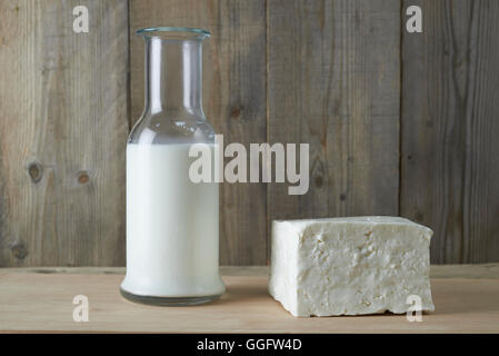 Frischer Schafskäse mit Flasche Milch auf einem Holztisch Stockfoto