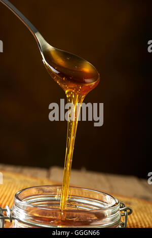 Honig tropft aus einem Löffel im Glas Stockfoto