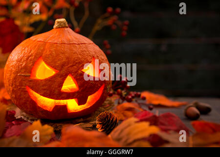 Brennen von Jack O'Lantern auf einem rustikalen Tisch mit herbstlichen Dekorationen, beleuchtet dunkel. Stockfoto