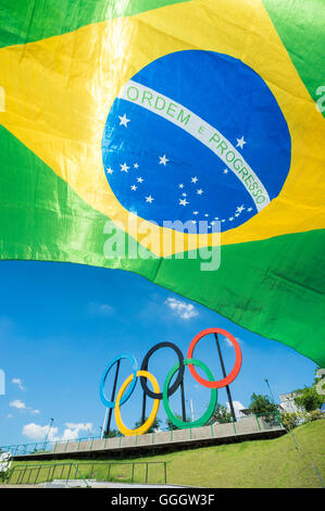 RIO DE JANEIRO - 18. März 2016: A Brasilien Flagge hängt vor einer Anzeige der Olympischen Ringe im Parque Madureira Park. Stockfoto