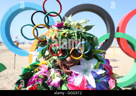 Ein Mann bedeckt in Blumen posiert für ein Foto vor der Olympischen Ringe an der Copacabana, Rio De Janeiro, Brasilien. Stockfoto