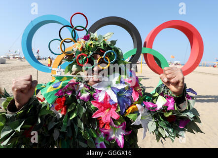 Ein Mann bedeckt in Blumen posiert für ein Foto vor der Olympischen Ringe an der Copacabana, Rio De Janeiro, Brasilien. Stockfoto