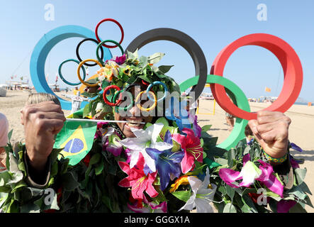 Ein Mann bedeckt in Blumen posiert für ein Foto vor der Olympischen Ringe an der Copacabana, Rio De Janeiro, Brasilien. Stockfoto