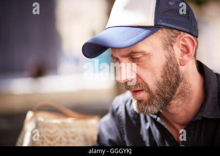Hipster mit Bart und Baseball Kappe sitzen in einem Straßencafé ernsthaft Stockfoto