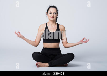 Fitte Frau in ihren 20ern, die yogische Meditation in Lotusposition praktiziert. In Fitnesskleidung sitzt sie auf dem Boden mit Kopierraum Stockfoto