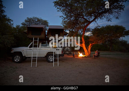 Familie um ein Lagerfeuer, Geländewagen mit Dachzelt im Vordergrund, Purros Camp, Hoarusib, Namib-Wüste, Namibia Stockfoto