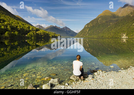 Reflexion der Berge im Lake Gunn, junge Frau sitzt an der See Ufer, Southland, Südinsel, Neuseeland Stockfoto