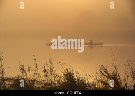 Ruderer Schiff im Nebel auf den Fluss, goldener Sonnenaufgang / Ruderboot Im Nebel Auf Dem Fluss, Goldener "Sonnenaufgang" Stockfoto