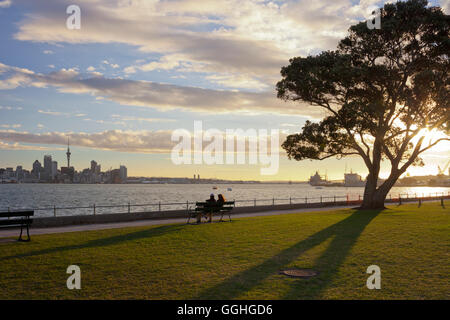 Paar, sitzen auf einer Bank, die auf der Suche an der Auckland Skyline, Stanley Bay, North Island, Neuseeland Stockfoto