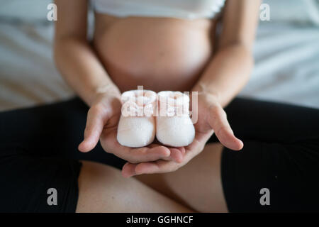 Schwangere Frau zeigt ihren Bauch und die weiße Wolle Schuhe des zukünftigen Kindes. Stockfoto