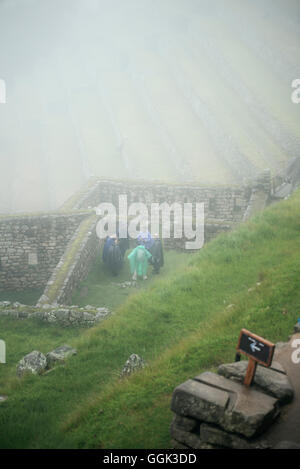 Gruppe von Touristen in Regenmäntel stehen dazwischen die Ruinen von Machu Picchu bedeckt im Nebel, Aguas Calientes, Peru, Süd-amerik. Stockfoto