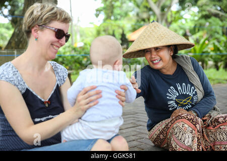 Balinesische Frauen, deutsche Mutter mit Baby, spielen, interkulturell, treffen Menschen vor Ort, einheimische, Familie Reisen in Asien, westliche ba Stockfoto