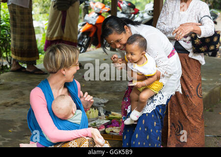 Balinesischen Mutter mit ihren Kindern spielen mit Baby der deutschen Mutter, Baby-Tragetuch, wickeln, Baby-Tragetuch bei ihrer Mutter, Baby 5 Monate Stockfoto