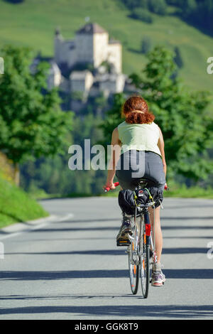Frau, Radfahren entlang der Straße, Schloss Tarasp im Hintergrund, Ftan Unterengadin, Engadin, Graubünden, Schweiz Stockfoto