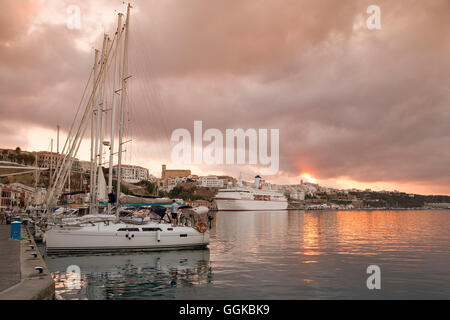 Segelyacht im Yachthafen und Kreuzfahrt Schiff MS Deutschland (Reederei Peter Deilmann) am Pier bei Sonnenuntergang, Mahon, Menorca, Balearen Stockfoto