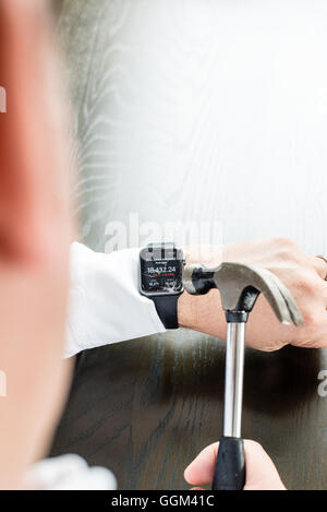Ostfildern, Deutschland - 31. Juli 2016: Ein Geschäftsmann trägt ein weißes Hemd ist die Apple Watch am Handgelenk mit einem Hamm zu zerstören Stockfoto