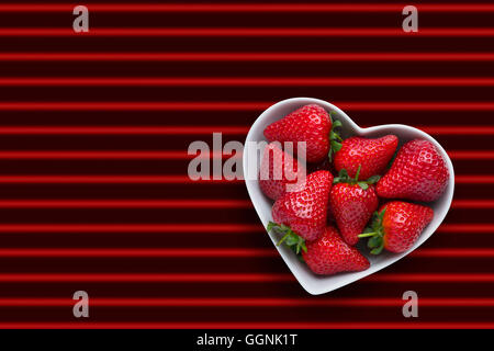 Erdbeeren in Herzform Schüssel auf rot gestreiften Hintergrund Stockfoto