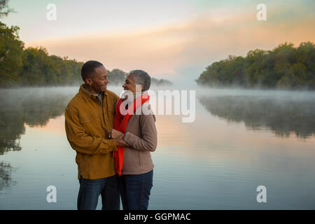 Älteres Ehepaar umarmt am nebligen River bei Sonnenaufgang Stockfoto