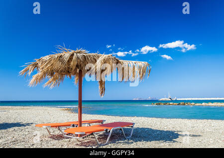 Strohschirm auf einem sandigen Strand in Griechenland. Liegestühle mit Sonnenschirmen am Strand in Insel Kreta. Stockfoto