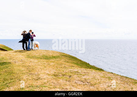 Kaseberga, Schweden - 1. August 2016: Echte Menschen im Alltag. Drei Personen und ein Hund steht am Hang mit dem Ozean werden Stockfoto