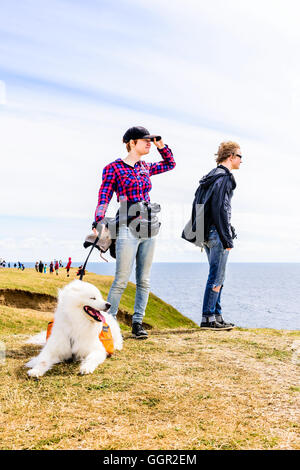 Kaseberga, Schweden - 1. August 2016: Echte Menschen im Alltag. Junge Erwachsene stehen auf windigen Hügel mit weißen Hund suchen Stockfoto