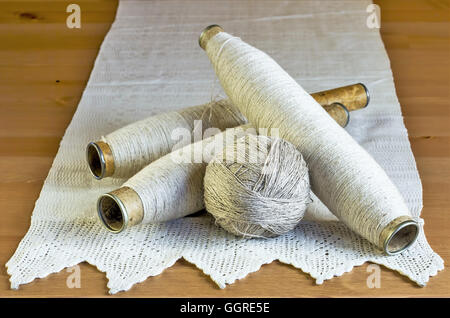 Vintage Spulen mit natürlichen Leinenfäden und handgemachten Spitzen Tischdecke auf einen hölzernen Hintergrund. Stockfoto