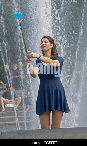 Eine attraktive Frau zu Besuch in New York unter einem Selfie am Brunnen im Washington Square Park in Greenwich Village. Stockfoto