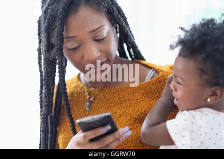 Schwarze Frau mit Baby-Tochter mit Handy Stockfoto