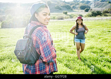 Lächelnd Mischlinge Schwestern Rucksackreisen in Feld in der Nähe von Berg Stockfoto