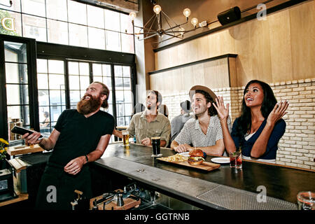 Lächelnd, Barkeeper und Kunden vor dem Fernseher in der Bar Stockfoto