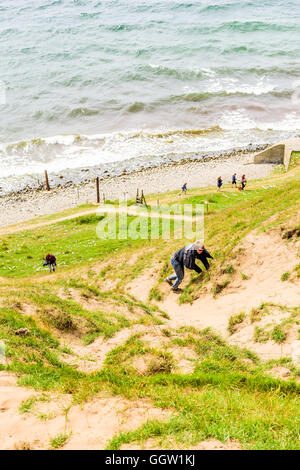 Kaseberga, Schweden - 1. August 2016: Junger Erwachsener Mann und Frau besteigen einen steilen sandigen Hügel aus das Meer. Realen Lebenssituation Stockfoto