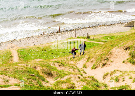 Kaseberga, Schweden - 1. August 2016: Junger Erwachsener Mann hilft einer Frau einen steilen sandigen Hügel aus das Meer zu klettern. Wirklichen Leben sit Stockfoto