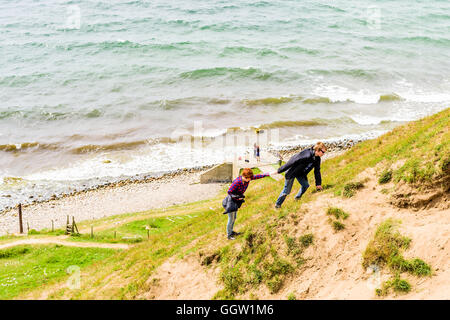 Kaseberga, Schweden - 1. August 2016: Junger Erwachsener Mann hilft einer Frau einen steilen sandigen Hügel aus das Meer zu klettern. Wirklichen Leben sit Stockfoto