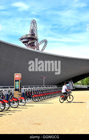 Person Reiten von Santander Fahrrad mieten docking-Station am Aquatic Centre mit Orbit Turm darüber hinaus im Queen Elizabeth Olympic Park Stratford in London UK Stockfoto