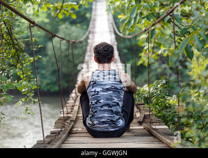 Teenager Junge sitzt auf einer Holzbrücke über den Fluss Stockfoto