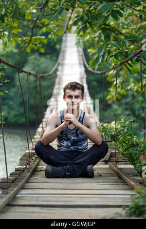 Teenager Junge sitzt auf einer Holzbrücke über den Fluss Stockfoto