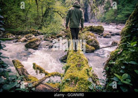 Mann Traveler Kreuzung Fluß auf Log Outdoor-Lifestyle Reisen überleben Konzept Stockfoto