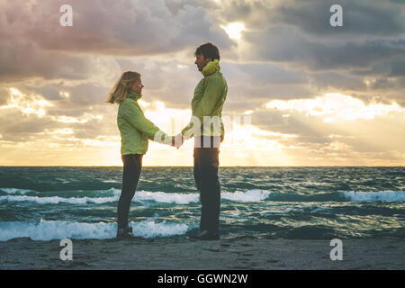 Junge Paar Mann und Frau halten Hände in Liebe Romantik im Freien mit Meer und Sonnenuntergang Natur Himmel Hintergrund Lebensgefühl Stockfoto