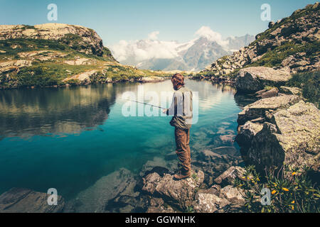 Junger Mann Angeln auf See mit Stab Berge Landschaft im Hintergrund Reisen Lifestyle Konzept Sommerurlaub Stockfoto