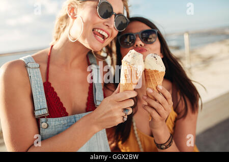 Porträt von zwei jungen Frauen stehen gemeinsam Eis essen. Glückliche junge Freundinnen im Freien. Stockfoto