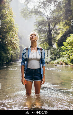 Attraktive junge weibliche Wanderer mit Rucksack in eine Wildnis-Stream stehen. Kaukasische junge Frau im Creek wegsehen. Stockfoto