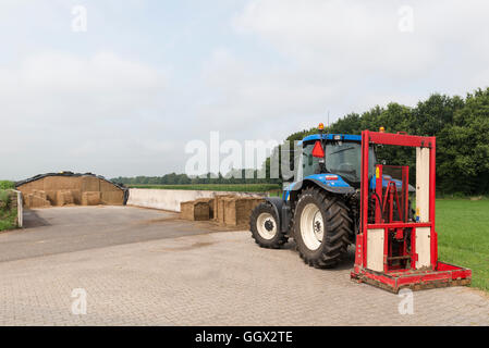 Blaue Traktor mit einem roten Ballen Hobel zum Abschneiden Silageballen Stockfoto