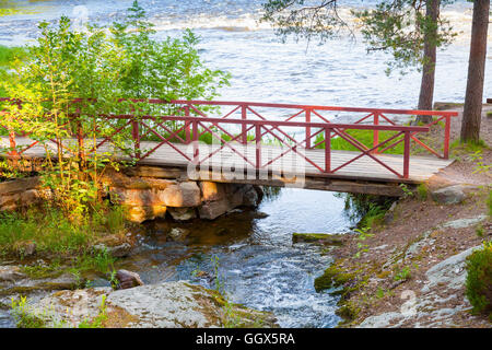 Kleine Holzbrücke mit rotem Geländer über Bach im Sommer. Kotka, Finnland Stockfoto