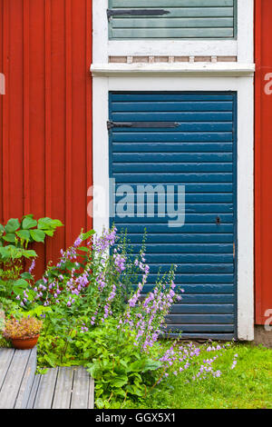 Porvoo, Finnland. Alte traditionelle finnische Architektur-Fragment. Dekorative Blumen in der Nähe von rote blaue Tür im roten Holzwand Stockfoto