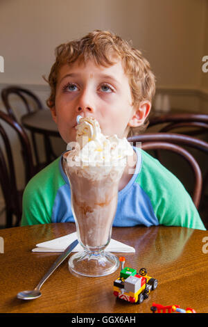 Sieben Jahre alten Jungen mit einer großen Schokoladen Milchshake, Totnes, Devon, England, Vereinigtes Königreich. Stockfoto