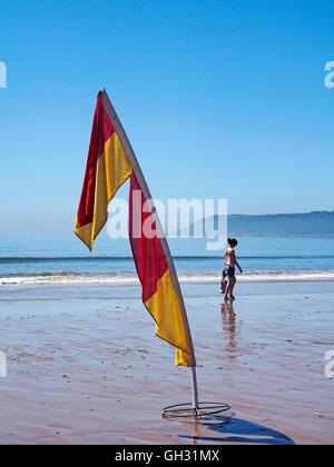 Rettungsschwimmer Markierungsfahnen zeigen patrouillierten gefährlich Strandbereich an drei Cliff Bay, Gower mit Menschen am Rand des Wassers. Stockfoto