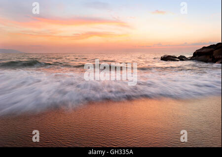 Ocean Sunset ist eine weiche Pastell farbigen Strandlage mit einem detaillierten Wolkengebilde und einer sanften Welle ans Ufer Rollen. Stockfoto