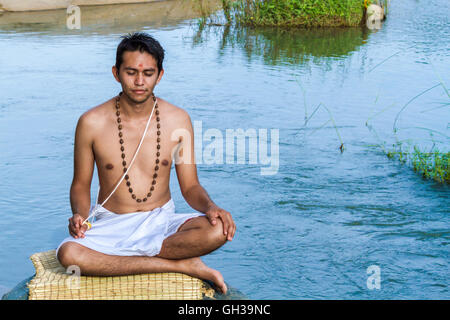 Ein junger Hindu Priester (Brahmanen) sitzt in der Meditation am Ufer eines Flusses. Stockfoto